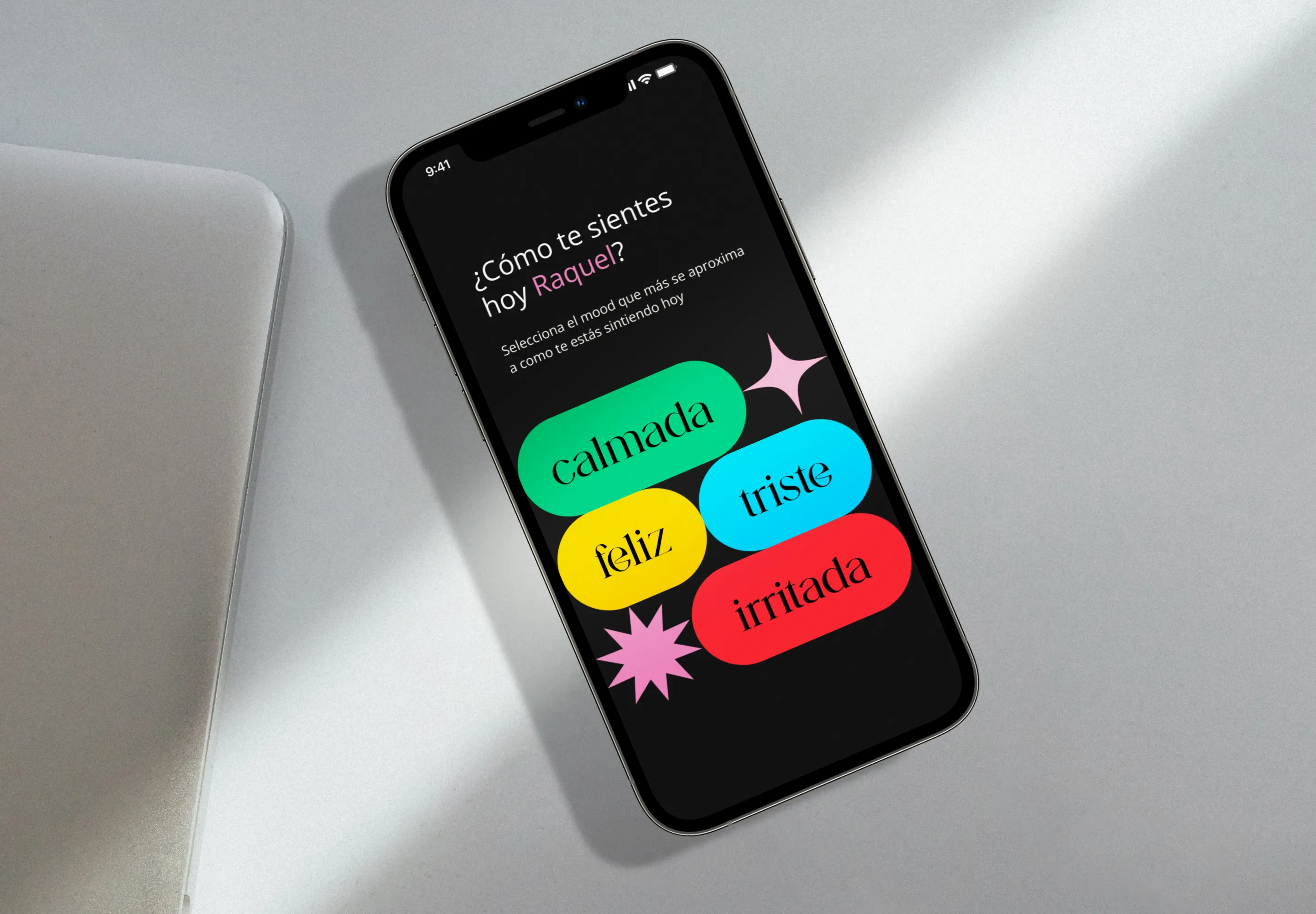 KooKoo app on a phone asking “¿Cómo te sientes hoy Raquel?” with colorful mood buttons